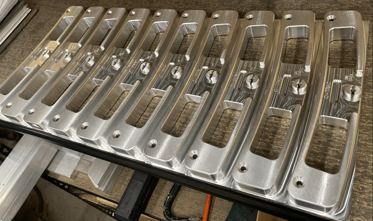 Precision-machined aluminum parts aligned on a workbench, showcasing their sleek design and pre-drilled holes for assembly.